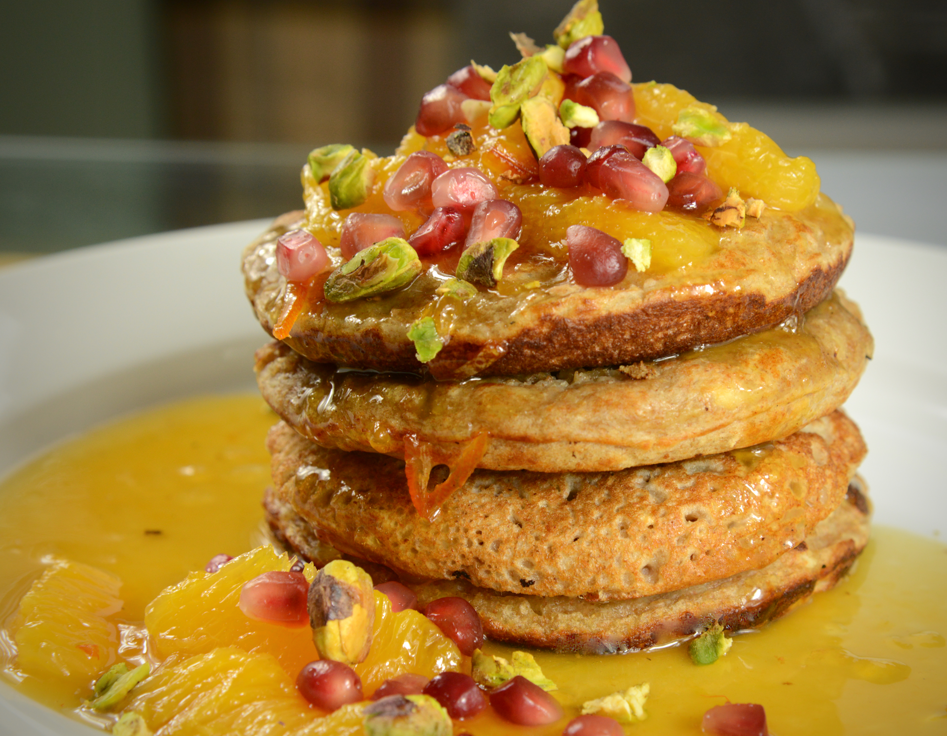 A delicious stack of Buckwheat-Banana pancakes topped with orange, pistachio and pomegranate