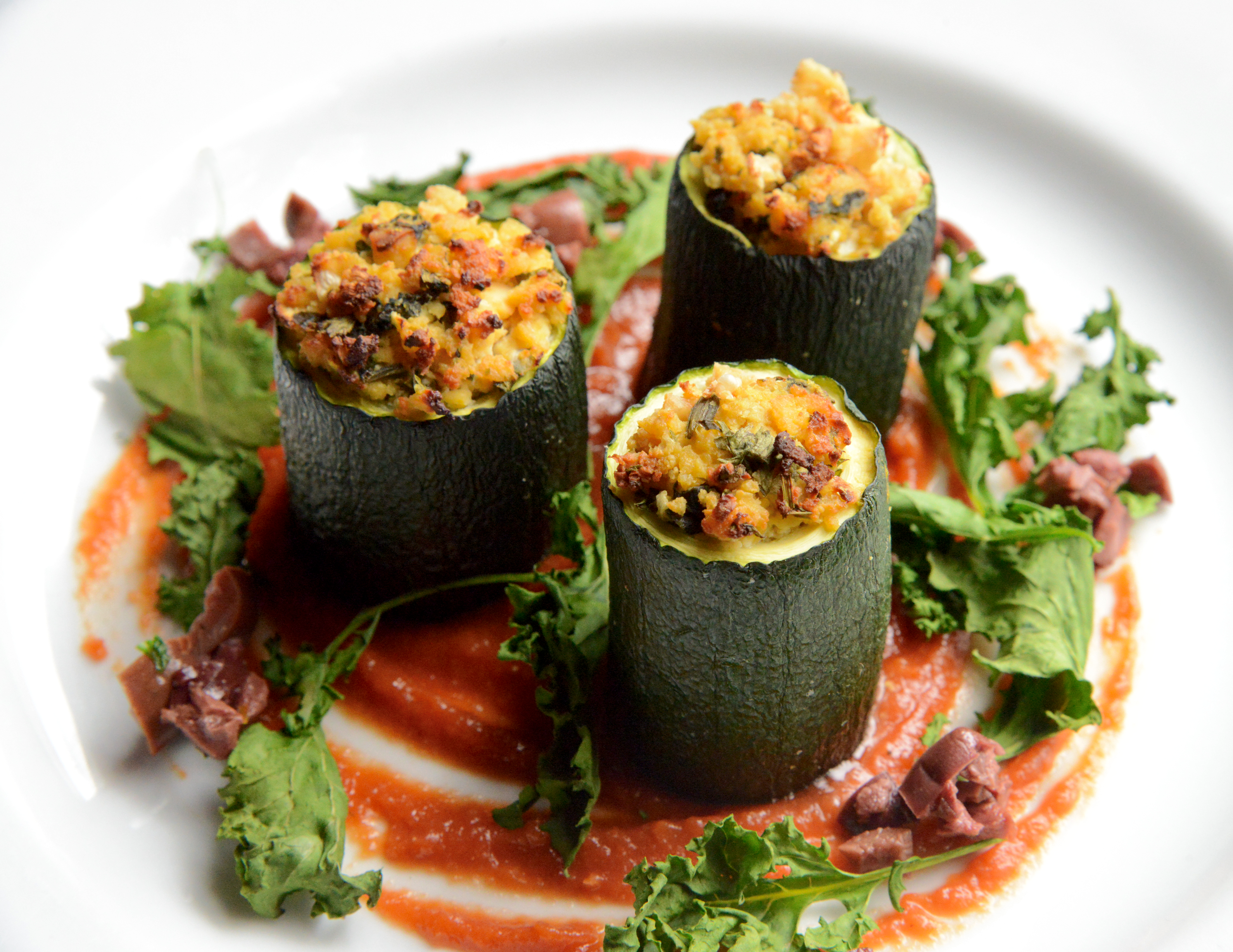 Zucchini cannelloni tubes filled with herby tofu ricotta on tomato & red pepper puree with crispy kale and black olives