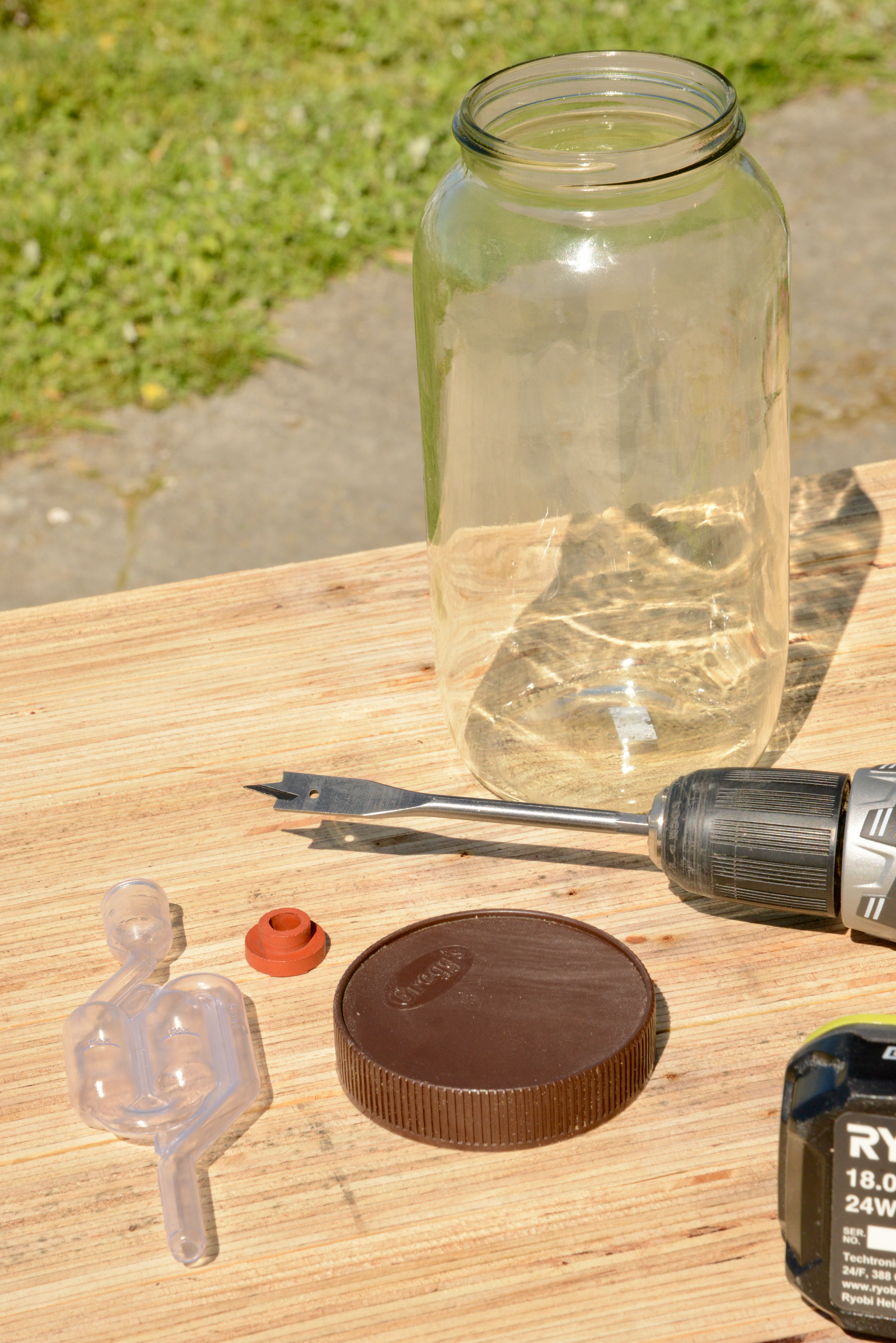 The parts to make your own fermenter, a lidded jar, airlock and airlock grommet and drill with bit