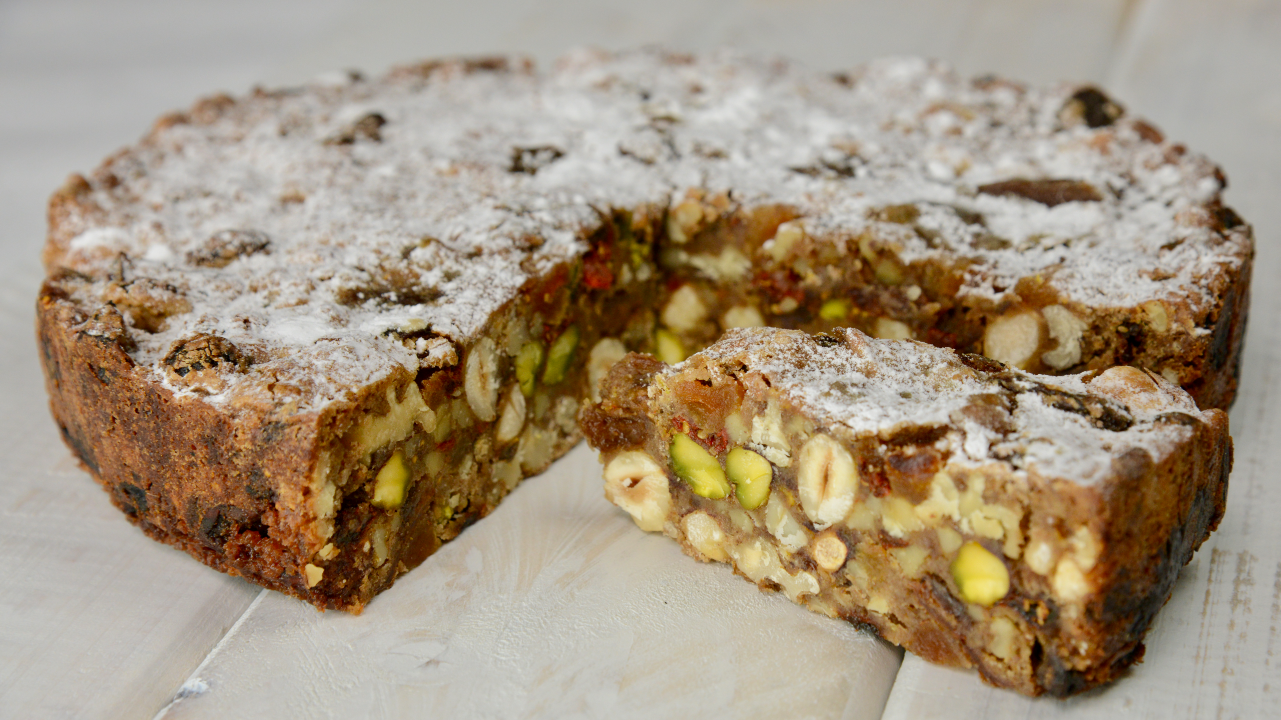 White plank board with a Whole panforte with wedge cut out deploying the selection of fruit and nuts used