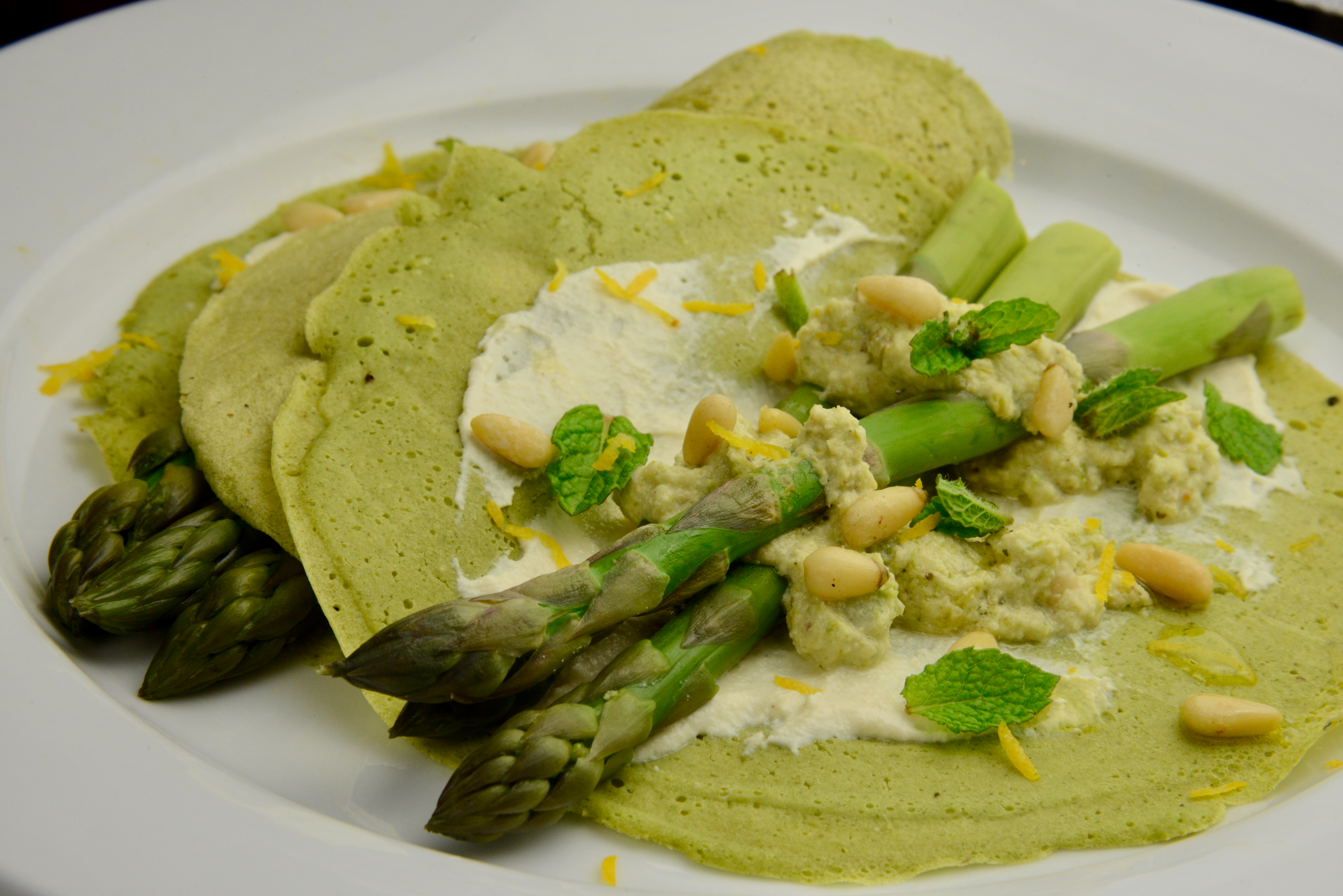 Fresh asparagus on sorrel crepes spread with cashew tofu cream and garnished with asparagus stem pesto, pine nuts and lemon zest
