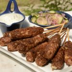 Platter with bbq'ed lentil and walnut kofte on skewers, herb cashew yoghurt and pickled cucumber and red onion