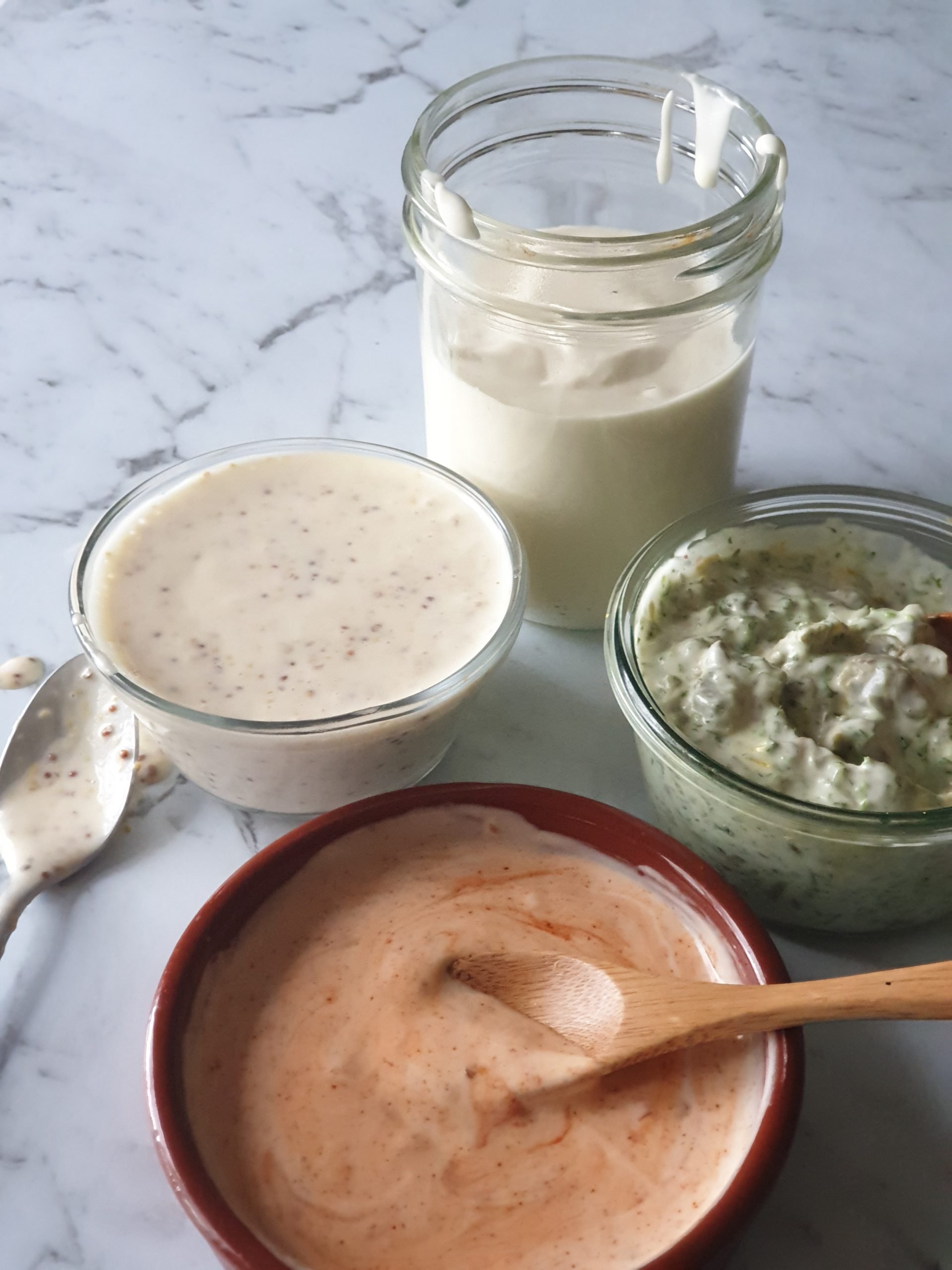 Jars of aquafaba mayonnaise and dressings on marble bench