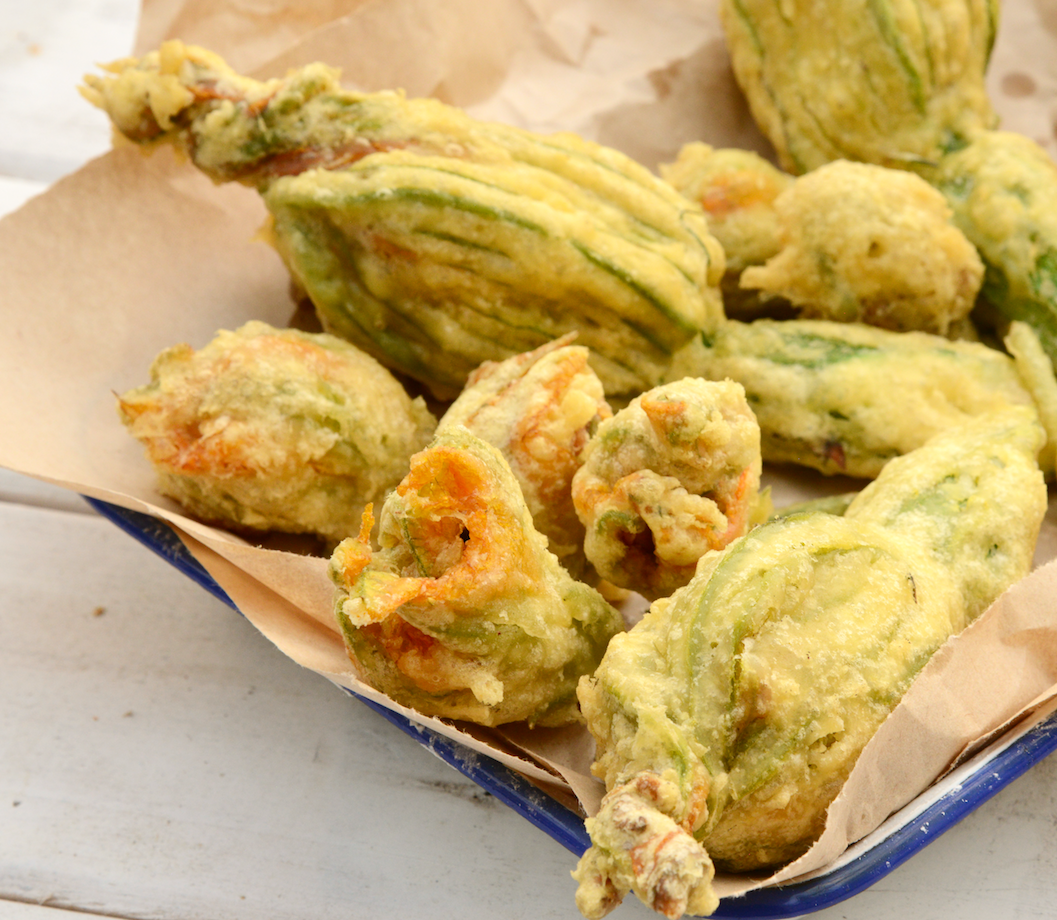 A brown paper lined tray of crispy, batter coasted stuffed zucchini flowers