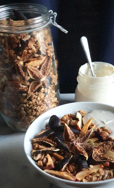 A bowl and jar of Autumn Foragers Granola with plant-based yoghurt on a marble bench