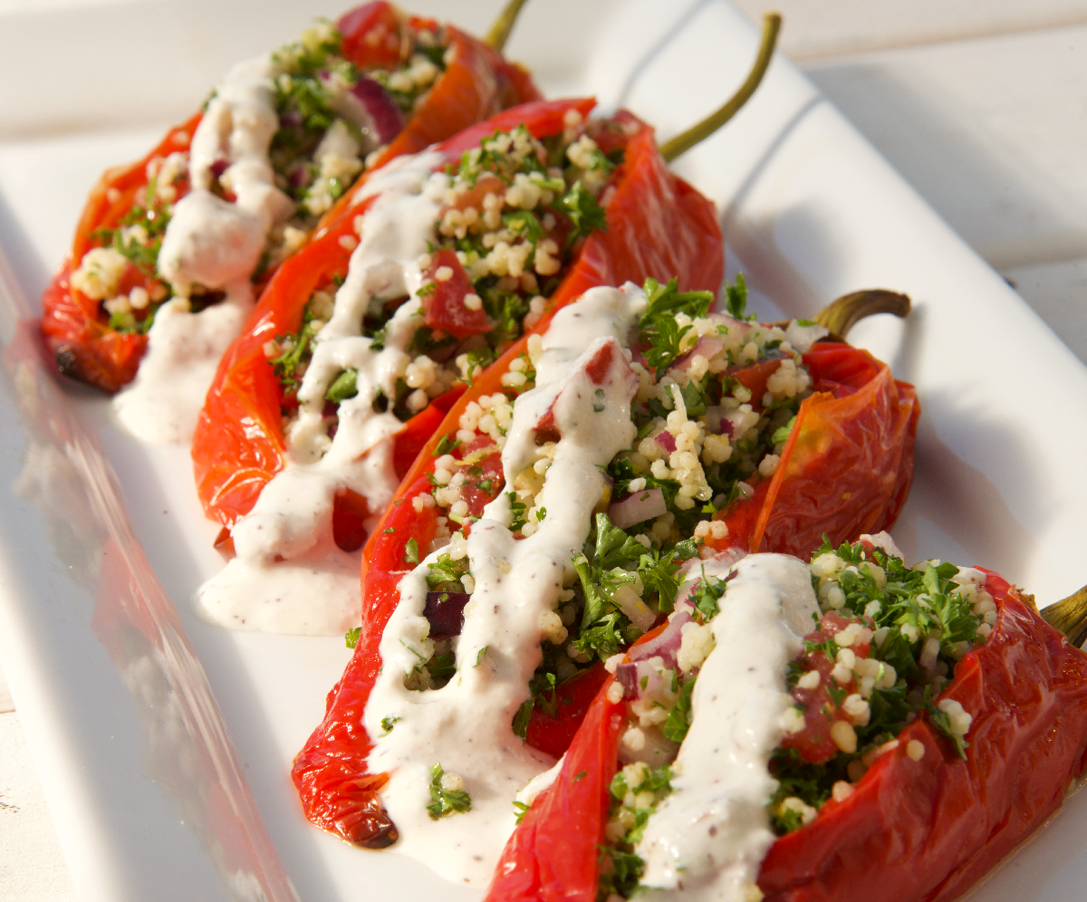 rectangle white platter with four tabbouleh stuffed peppers drizzled with sumac lemon yoghurt