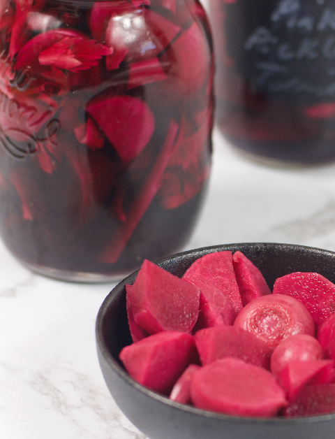 A bowl of pink pickled turnips with jars of preserved pickled turnips