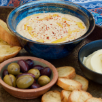 Metal tray with bowl of sesame free Hummus, olives and crostini