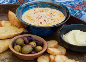 Metal tray with bowl of sesame free Hummus, olives and crostini