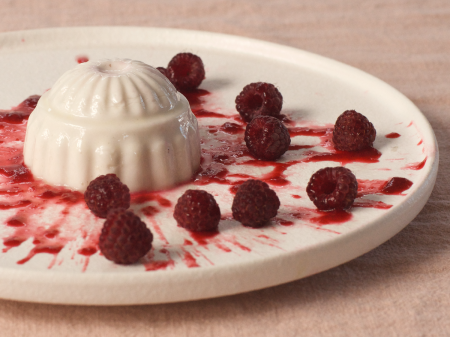 White plate with a splatter of raspberry coulis, a coconut panna cotta and fresh raspberries