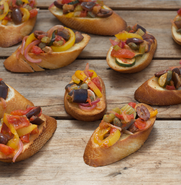 Brown wooden board with crostini and colourful caponata antipasto