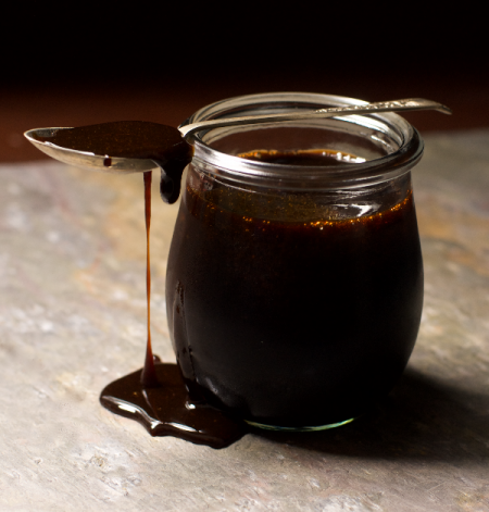 A jar of Date syrup with a drizzle and teaspoon