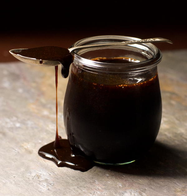 A jar of Date syrup with a drizzle and teaspoon